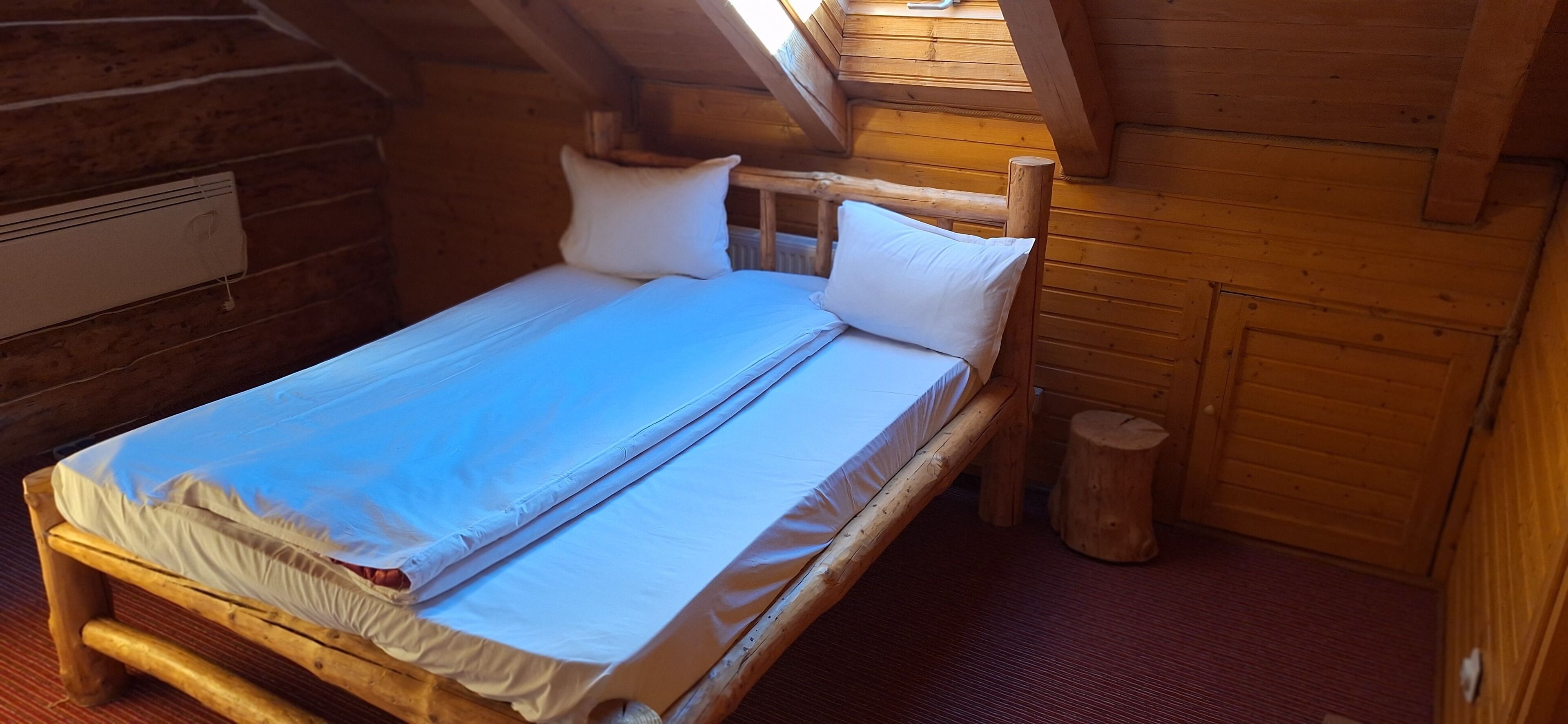 A wooden bed with white linens in a cabin-style room with a sloped ceiling.