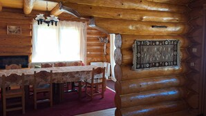 A log cabin interior with a dining table, chairs, a fireplace, a chandelier, and a patterned rug. - Chalet Rosehip Flowers 4-6 Traveling (Rasnov)