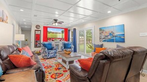 A spacious living room with a large TV, leather sofas, and a colorful rug. - The Plash Pad - 4-bedroom w/Pool in Gulf Shores!! Your Vacation Destination!! (Gulf Shores)