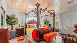 A four-poster bed with a wooden canopy, a bench, a nightstand, and a dresser in a room with a tiled floor and a patterned rug. - The Plash Pad - 4-bedroom w/Pool in Gulf Shores!! Your Vacation Destination!! (Gulf Shores)