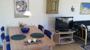 Un coin repas avec une table en bois, des chaises bleues, un téléviseur et un meuble.