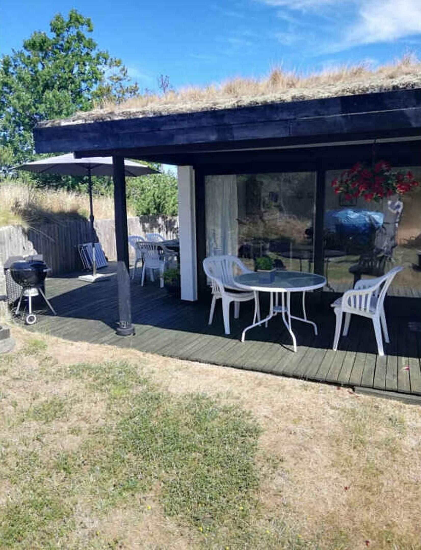 Eine überdachte Terrasse im Freien mit Tisch, Stühlen, einem Grill und Blick auf die umliegende Landschaft.