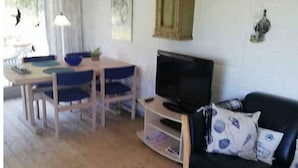 Un salon avec un canapé noir, un téléviseur, une table à manger en bois avec des chaises bleues et un tapis à motifs.