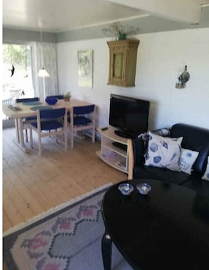 A living room with a black sofa, a television, a wooden dining table with blue chairs, and a patterned rug. - 4 Star Holiday Home in Laeso (Læsø)