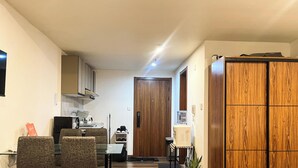 A compact kitchen with a dining area, a wooden wardrobe, and a small table with chairs.