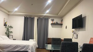 A hotel room with a bed, a desk, a chair, a TV, and a shelf with decorative items.