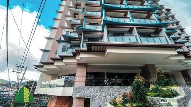 A multi-story building with balconies, a stone facade, and a view of the surrounding area.