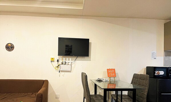Ein Wohnzimmer mit einem an der Wand befestigten Flachbildfernseher, einem Glastisch, einem braunen Sofa und einem kleinen Schild auf dem Tisch.