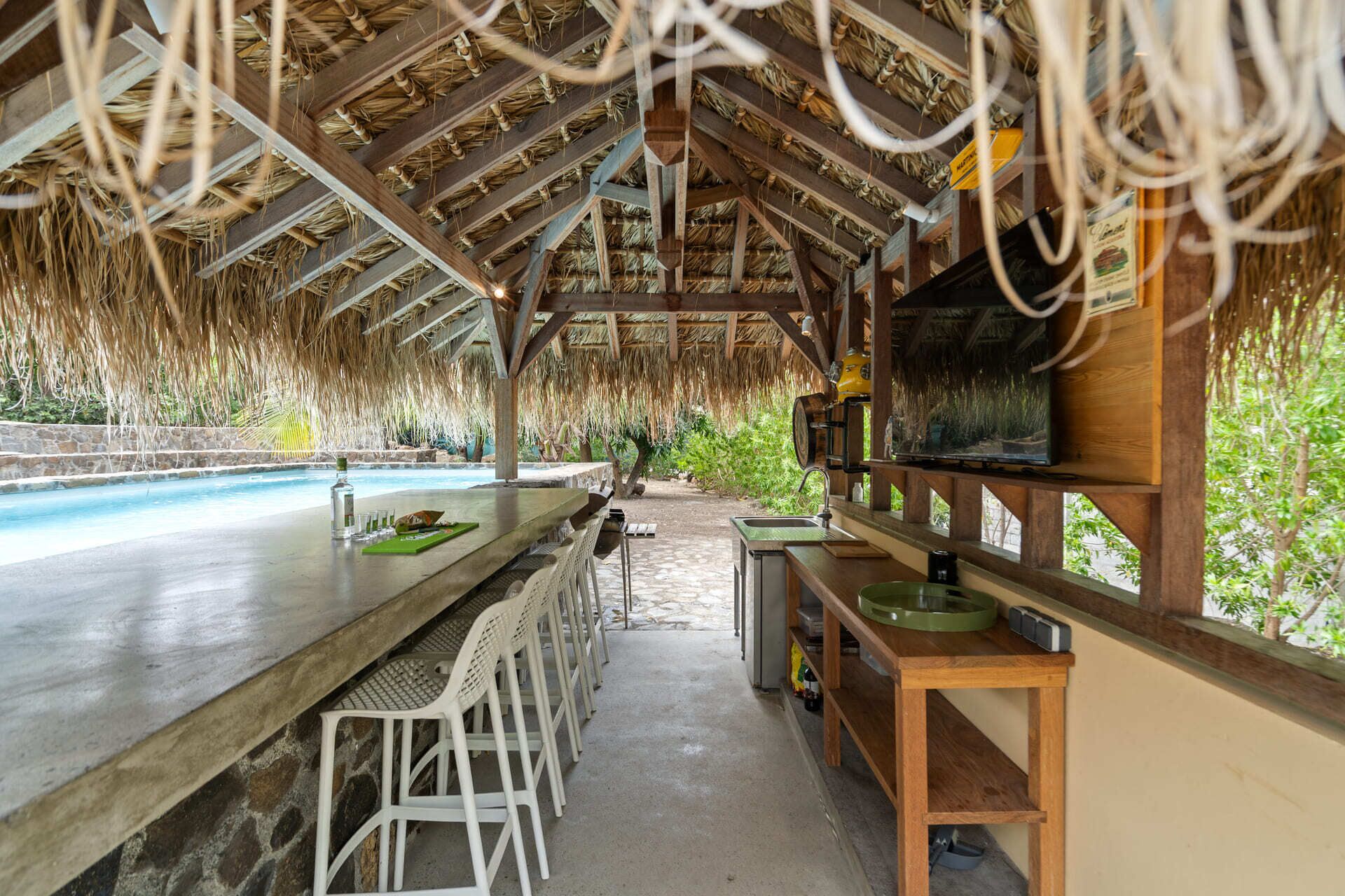 A covered outdoor bar area with a pool, wooden ceiling, and bar stools.