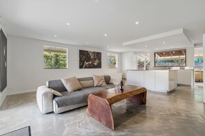 Ein modernes Wohnzimmer mit einer Couch, einem Holztisch und einer Küchenzeile mit weißer Arbeitsplatte.