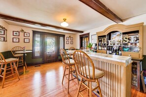 A bar area with wooden chairs, a bar counter, and a shelf with bottles. - The Mystic Inn | Wine and Cheese Shop Downstairs | Downtown LG (Lake Geneva)