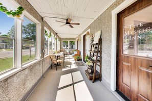 A covered porch with ceiling fans, large windows, and a wooden door labeled 'The Mystic Inn.' - The Mystic Inn | Wine and Cheese Shop Downstairs | Downtown LG (Lake Geneva)