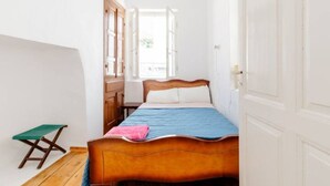 A narrow room with a bed, a small table, and a window with a view. - Cosy Rooms in a Traditional House in the 'Marble Village' on the Island of Naxos (Naxos)