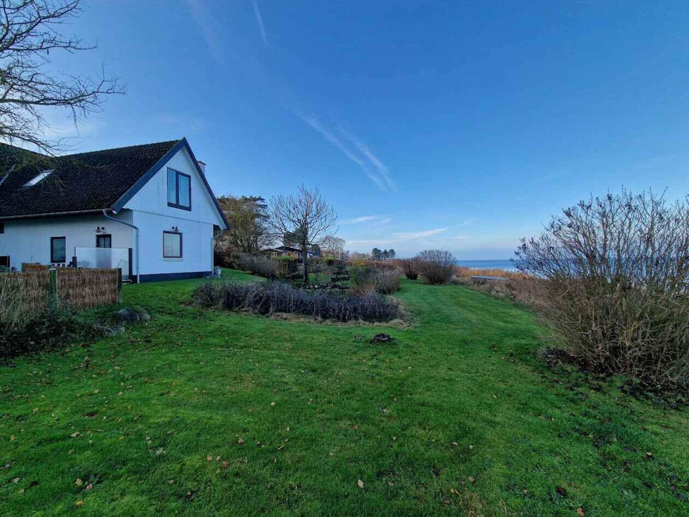 A white house with a sloped roof, a grassy yard, and a view of the sea.