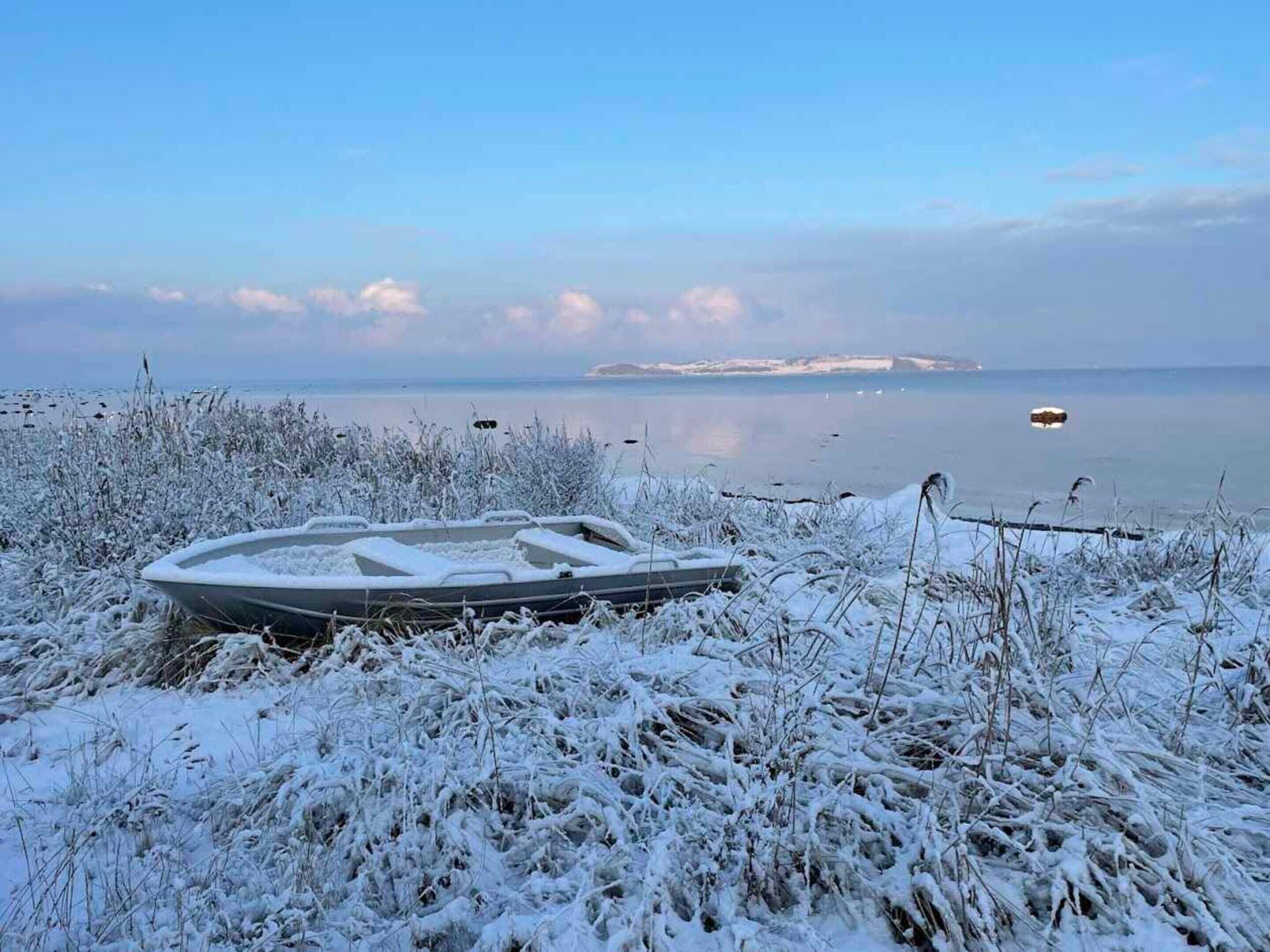 A boat on a snow-covered shore with a calm body of water and distant land in the background.