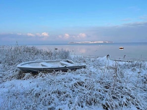 Um barco numa margem coberta de neve, com águas calmas e terra ao fundo.