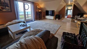 A spacious living room with a large television, a cozy fireplace, and a view of the outdoors. - 4 Star Holiday Home in Follenslev (Follenslev)