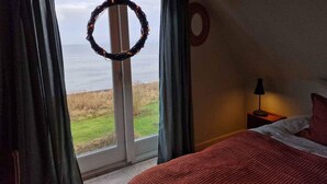 A bedroom with a bed, a nightstand, a lamp, a window with curtains, and a view of the outdoors. - 4 Star Holiday Home in Follenslev (Follenslev)