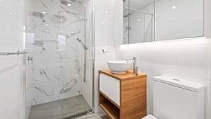 Ein modernes Badezimmer mit einer gläsernen Duschkabine, einem hölzernen Waschtisch mit weißem Waschbecken und einer weißen Toilette.