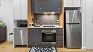 Eine kompakte Küche mit Geschirrspüler, Backofen und Kühlschrank, die ein modernes Design mit dunklen Schränken und einer Holzvertäfelung an der Wand aufweist.