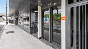 Ein moderner Gebäudeeingang mit Glastüren, einem Metallgitter und einem sichtbaren Adressschild.