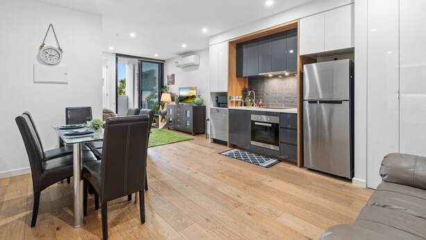 Eine moderne Küche mit Essbereich, Holzboden und einem grauen Sofa.