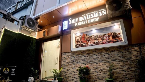 The exterior of Shiv Darshan P. Guest House with a framed cityscape picture, air conditioning units, and potted plants. - Shiv Darshan P Guest House (Varanasi)