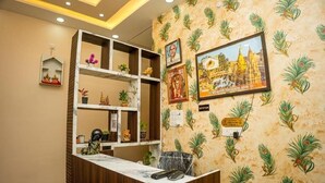 A reception desk with a wooden finish, a marble counter, and a wall adorned with framed pictures and a peacock pattern. - Shiv Darshan P Guest House (Varanasi)