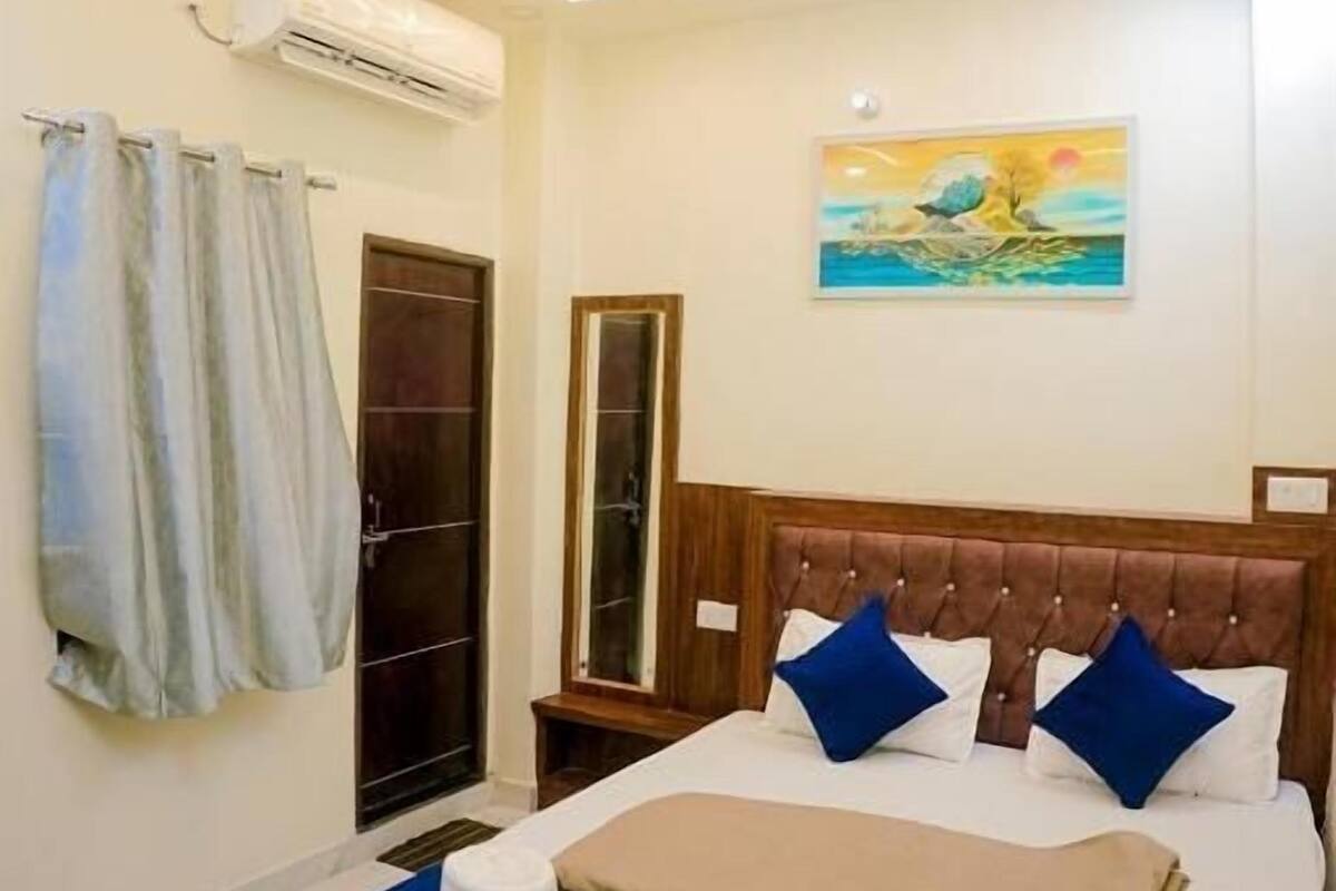 A bedroom with a bed, a ceiling fan, an air conditioning unit, a painting, and a wooden wardrobe.