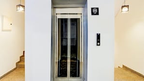 Un ascenseur doté d’une porte en verre, d’un panneau indiquant qu’il s’agit d’un ascenseur, et de deux lampes suspendues.
