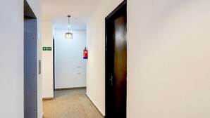 Un couloir étroit avec un mur blanc, une porte en bois et un extincteur fixé au mur.