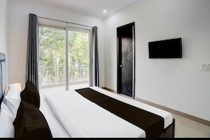 Ein Hotelzimmer mit Bett, Wandfernseher und Vorhängen am Fenster.