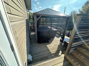 Een overdekt terras buiten, met een barbecue, houten omheining en een houten dek.