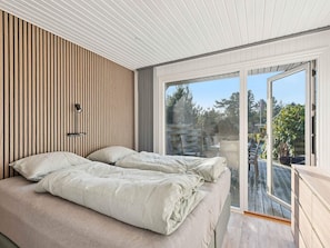 A modern bedroom with a bed, a wall-mounted lamp, and a large sliding glass door leading to an outdoor deck. - 4 Star Holiday Home in Hemmet (Hemmet)