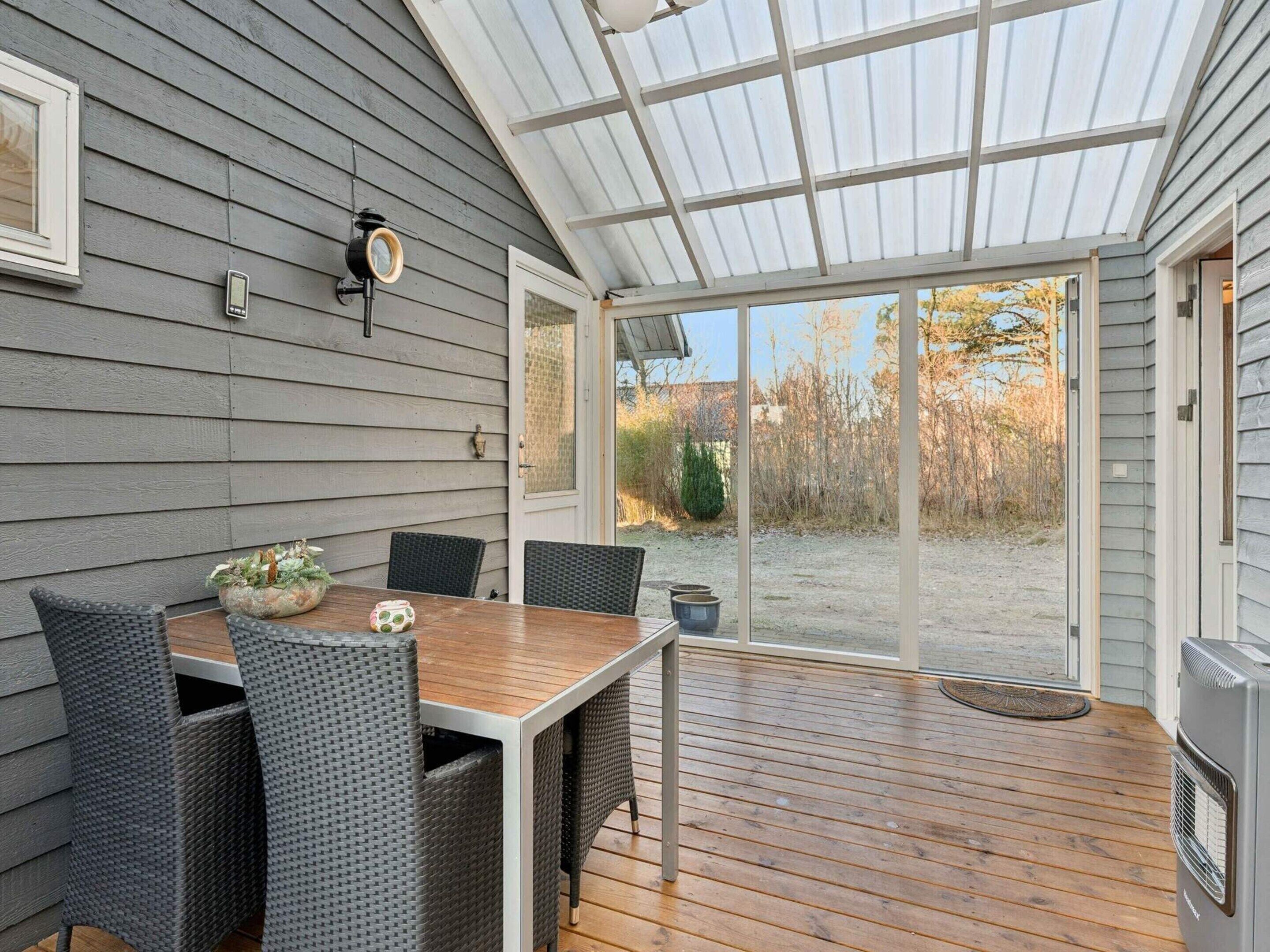 A covered patio with a wooden table and wicker chairs, a thermostat, and a view of the outdoors.