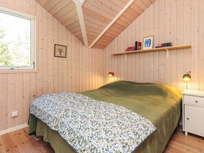 Ein Schlafzimmer mit einem Bett, einem Nachttisch, einem Regal mit Büchern, einem gerahmten Bild und einem Fenster.