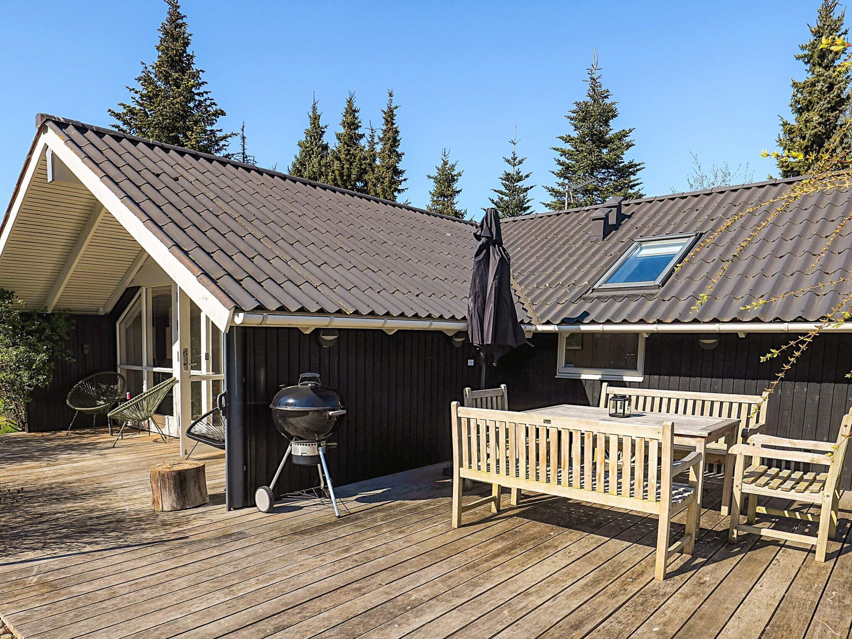 Une terrasse en bois avec un barbecue, des sièges d’extérieur et un espace abrité doté d’une fenêtre.