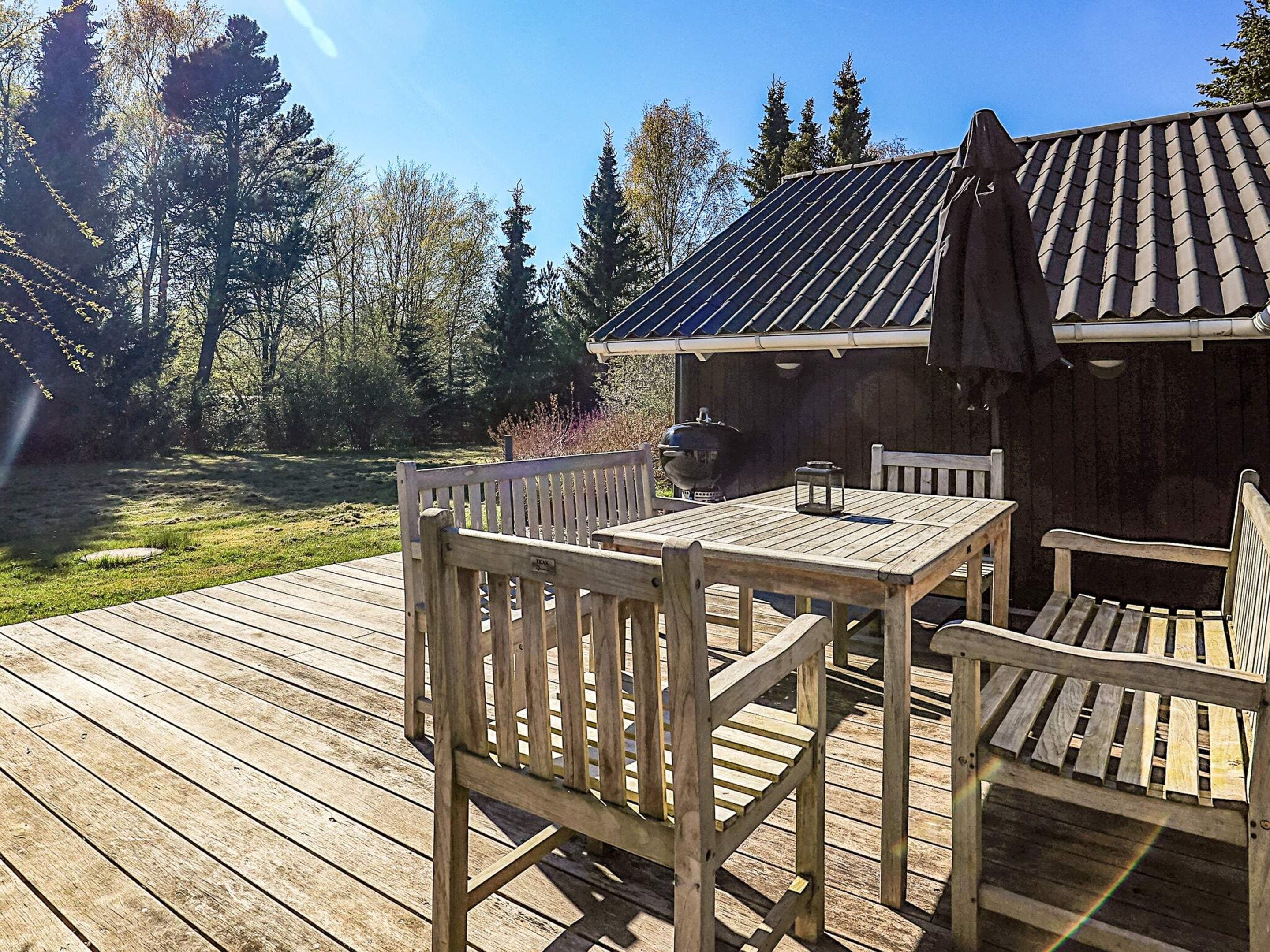 Une terrasse en bois avec une table et des chaises, un barbecue et un espace abrité avec un toit.