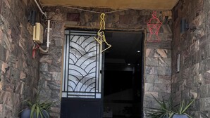Entrada d'un edifici amb parets de pedra i una reixa metàl·lica decorativa, escales que hi condueixen i plantes en testos a ambdós costats.