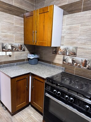 Cuina amb armaris de fusta, taulell de granat i estufa, i rajoles decoratives.