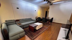 Un saló modern amb un sofà modular, una taula de centre, una zona de menjador amb cadires i un televisió de pantalla plana.