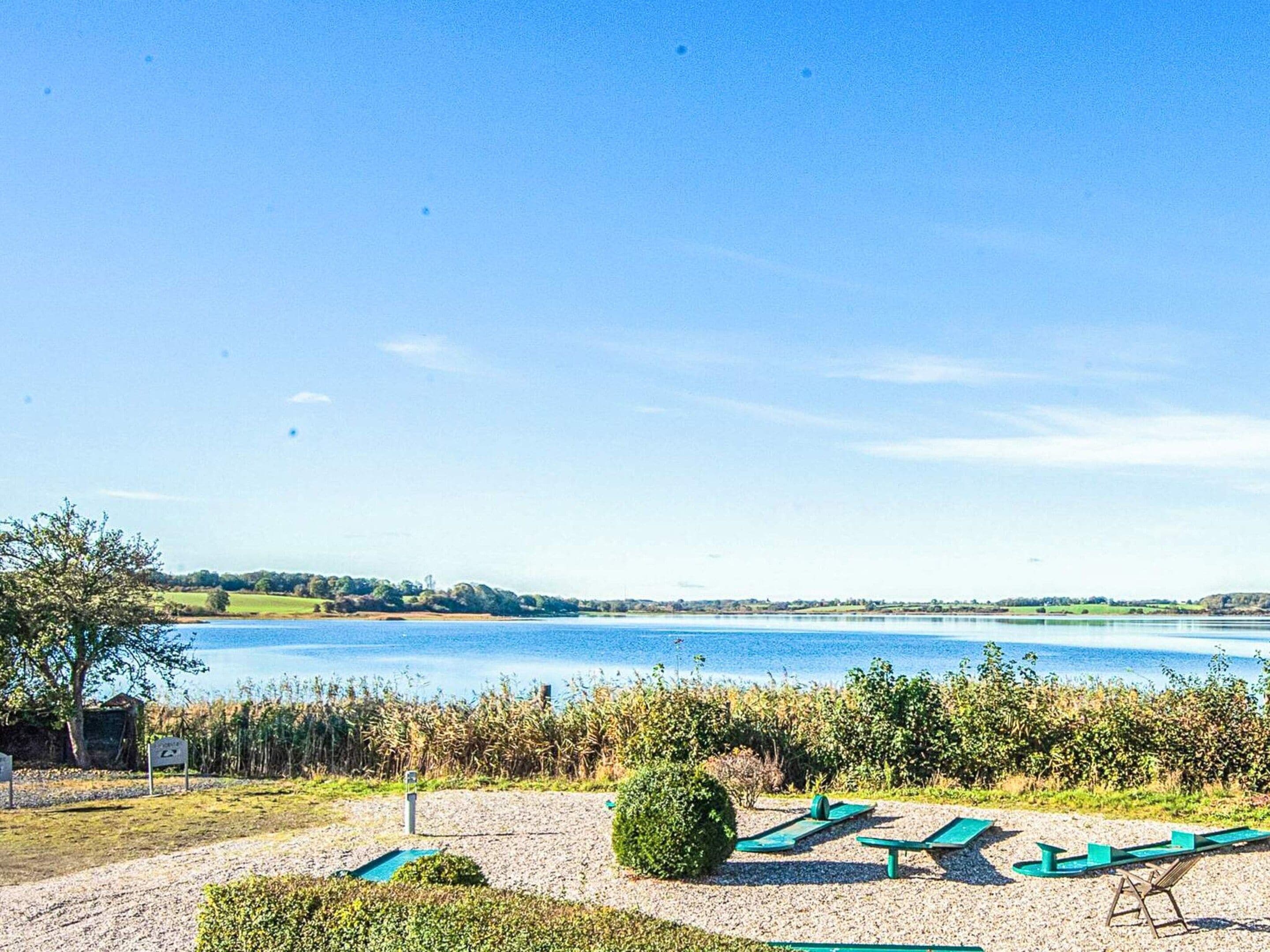 A lakeside view with a gravel path leading to a row of green lounge chairs.