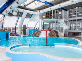 Una piscina interna con uno scivolo, una piccola cascata e una scala che conduce a un piano superiore.