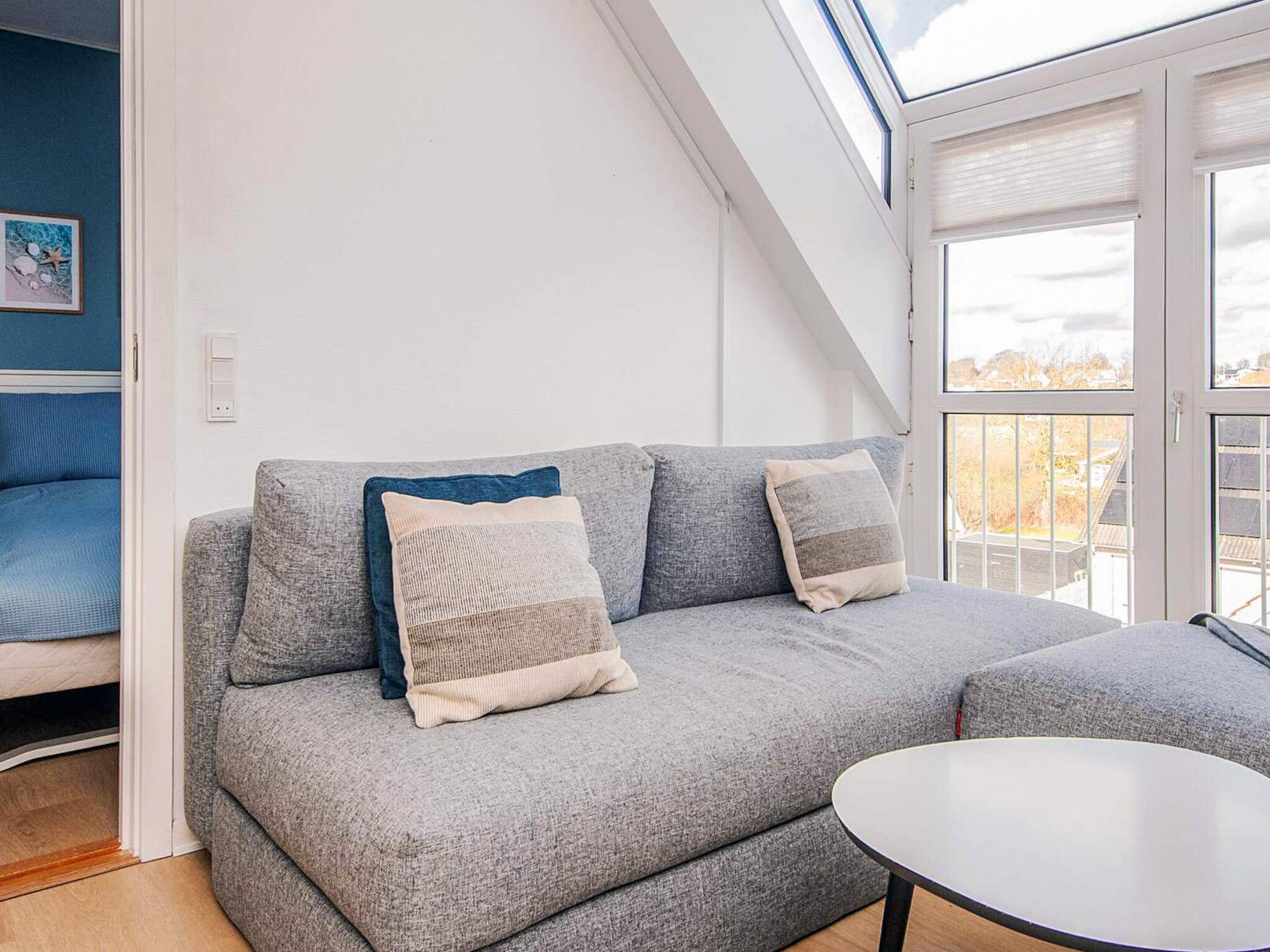 A modern living room with a grey sofa, two cushions, a round coffee table, and a skylight above.