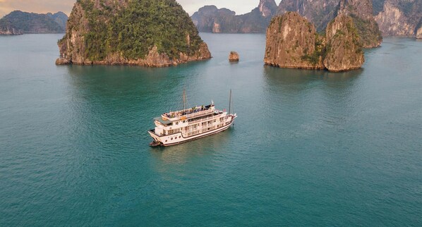 Un grand bateau à plusieurs ponts, entouré d’une eau calme et d’îles rocheuses.