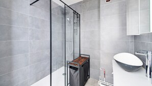 Ein modernes Badezimmer mit einer Duschkabine aus Glas, einem Holzregal, einem weißen Waschbecken und einer großen Badewanne.