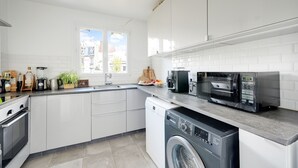 Eine moderne Küche mit weißen Schränken, einem Geschirrspüler, einer Waschmaschine, einer Kaffeemaschine und einer Mikrowelle.