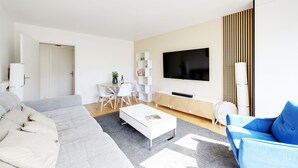 Ein modernes Wohnzimmer mit einer Couch, einem Couchtisch, einem Fernseher und einem Essbereich mit Stühlen und Tisch.