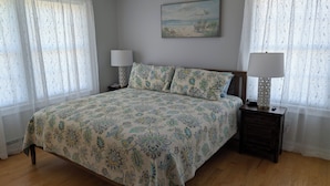 Un dormitorio con cama, dos mesitas de noche con lámparas, un cuadro en la pared y cortinas de encaje.