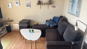A modern living room with a dark grey sofa, a white coffee table, and a small side table. There are framed pictures on the wall and a shelf with decorative items. - 4 Star Holiday Home in Tranekaer (Tranekaer)